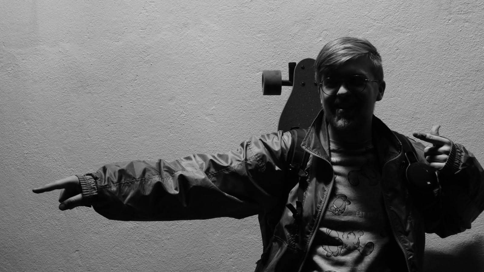 A monochromatic portrait of Kasper Bielecki with a longboard strapped to his backpack.